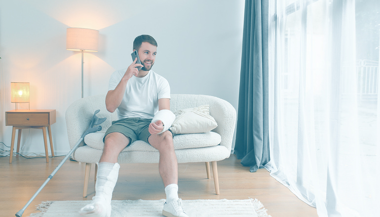 hombre sentado em el sofa después de tener un accidente de tráfico tiene el brazo y la pierna rota, es cuándo debe llamar a un abogado tras el accidnete de tráfico que ha sufrido